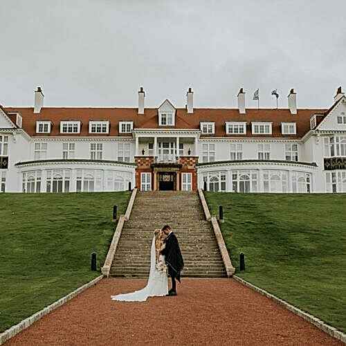 a married couple standing in front of large steps leading to a hotel